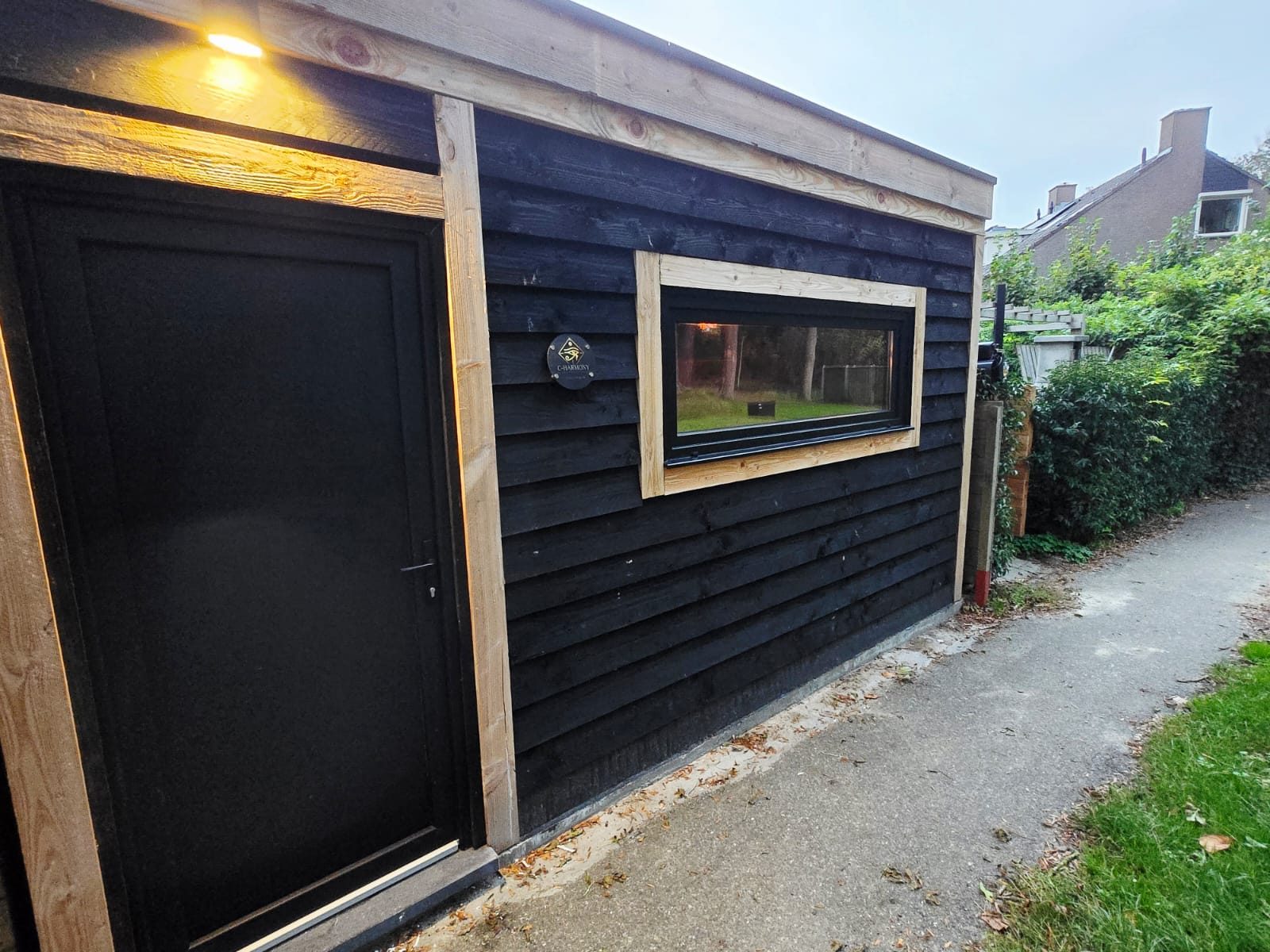 De zwart houten praktijkruimte met een breed raam, aan het tuinpad