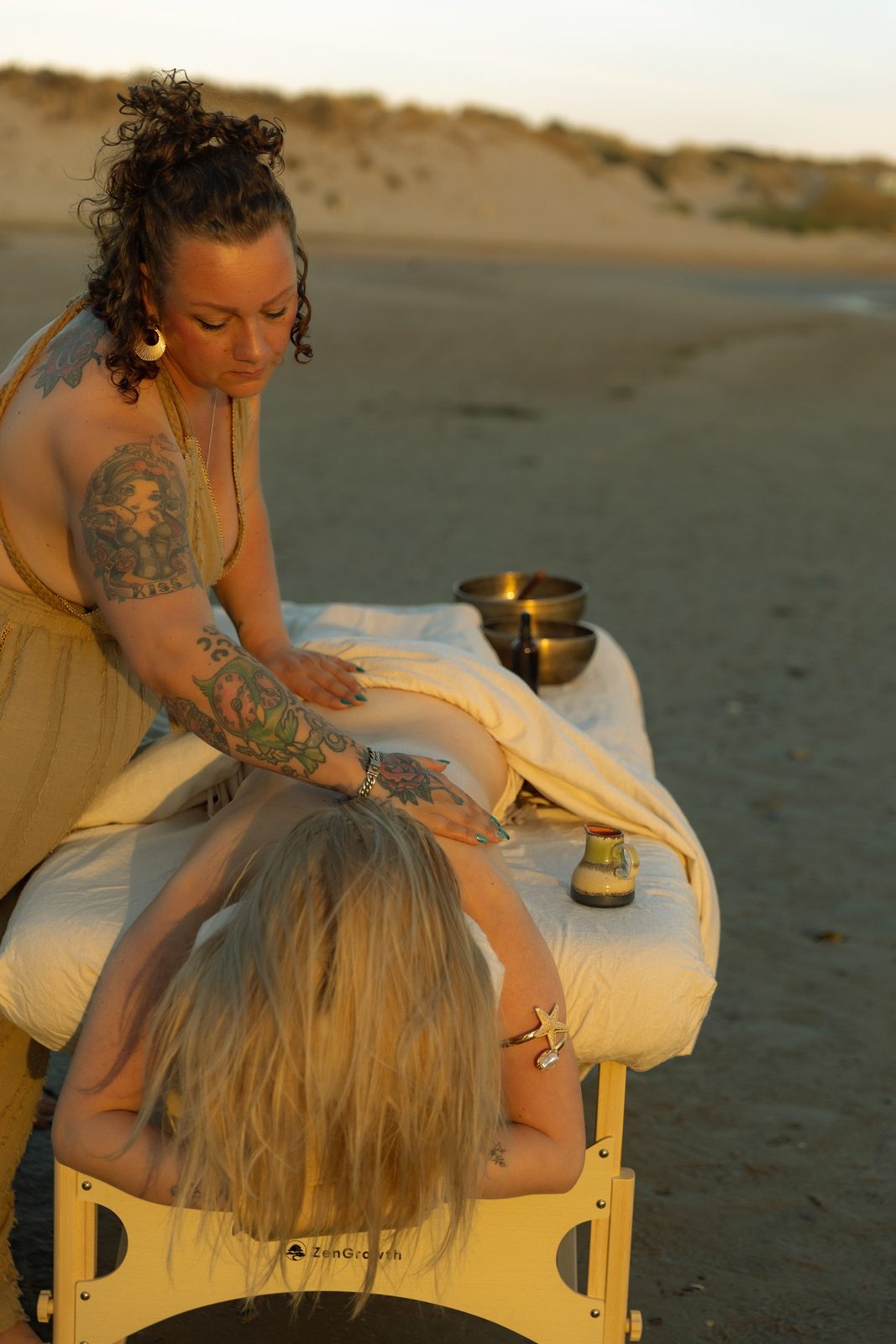 Chantal masseert een cliënt op een massagetafel op het strand bij zonsondergang